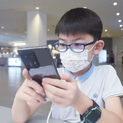 En pojke med glasögon använder en mobiltelefon.