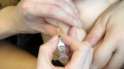 Ett litet barn med napp i munnen får en vaccinspruta.