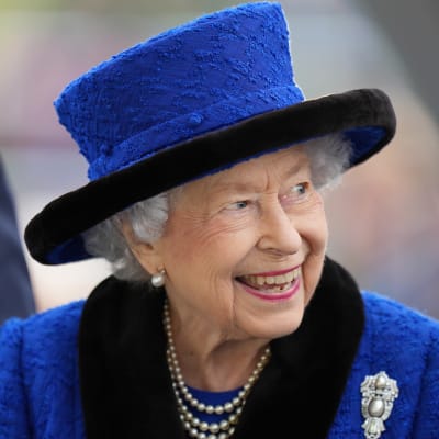 Drottning Elizabeth ler och tittar åt sidan. Hon har på sig en blå kavaj och en hatt i samma nyans. 