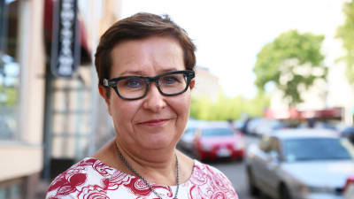 En nöjd kvinna från axlarna uppåt. I bakgrunden syns en somrig gata och några bilar.
