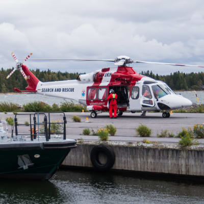 En sjöräddningshelikopter står parkerad på en pir. I förgrunden en förtöjd gränsbevakningsbåt.