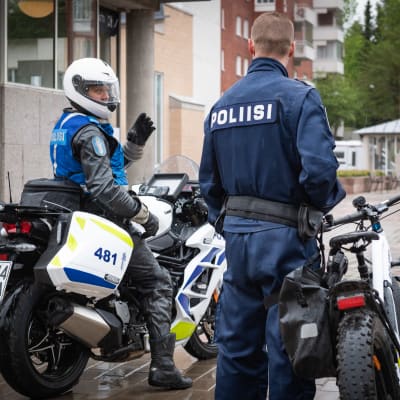 En polis sitter på en motorcykel, medan en annan polis står vid en cykel.