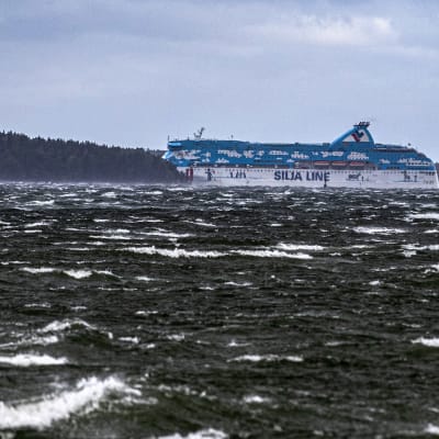 Tallink Siljas blåvita passagerarfartyg Galaxy försvinner bakom en ö under en höststorm med vita toppar på vågorna.