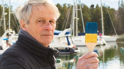 Ole Sandman med målarpensel i handen i hamnen med segelbåtar