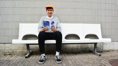 Kasper Strömman läser sin bok på vit bänk
