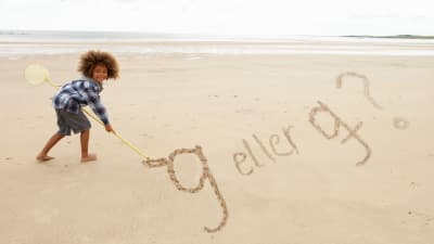 Liten flicka skriver g eller g på två olik sätt i sanden med en pinne