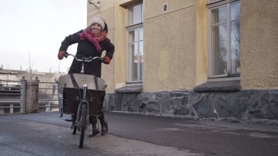 Linda Sundberg med cykel och halsduk framför gult stenhus.