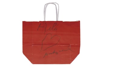 Röd tygkass med texten Heli ett hjärta och signaturen Andy Warhol som Warhol gett åt Heli vaaranen.