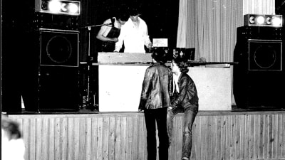 En mycket ung Måns Strömberg med kompis som dj på svartvitt foto. Två tjejer står framför scenen.