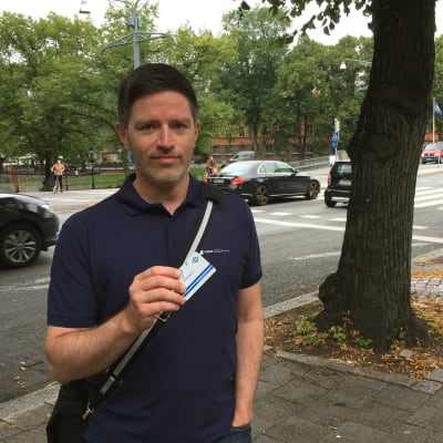 Mathias Johnson står vid gatan och håller upp sitt busskort.