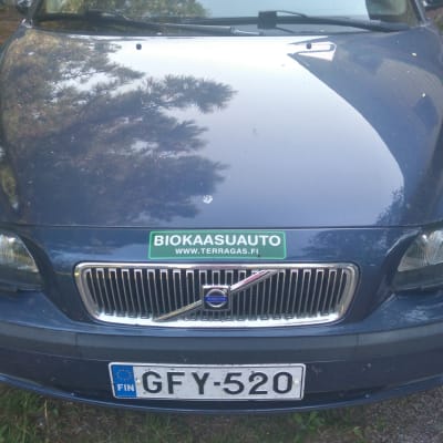 Uudehko sininen Volvo edestäpäin kuvattuna. Auton konepellissä on vihgreä tarra, jossa lukee" biokaasuauto".