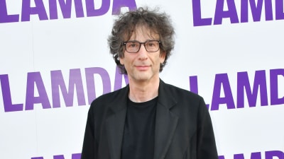 Neil Gaiman klädd i svarta kläder. Står framför en vägg som det står LAMDA på.