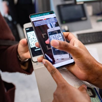 En kvinna visar upp ett covidintyg från telefonen, medan en annan scannar av det.