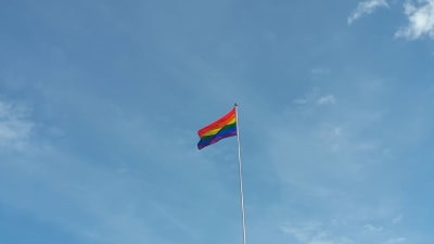 Prideflagga vajar i vinden mot en blå himmel.