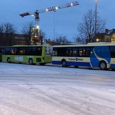 Kuvassa linja-autoja jonossa lumisella torilla