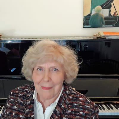 Pianisti Meri Louhos kotonaan pianon edessä, taustalla hänen maalamansa taulu pianistista