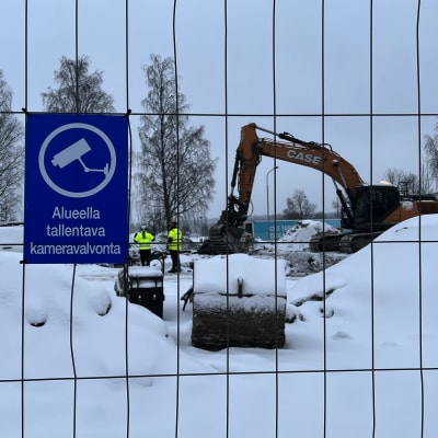 Byggarbetsplats med skylt som varnar utomstående för att röra sig på området. I bakgrunden syns grävmaskin.