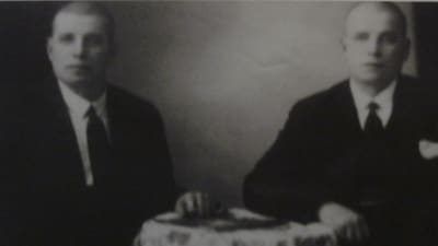 Tvillingbröder Hjalmari och Ilmari Mäkelä sitter vid ett bord på ett svartvit fotografi. 