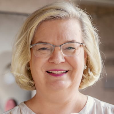 En bild på Gunvor Kronman som ler mot kameran. I bakgrunden syns ett konstverk i runda former.