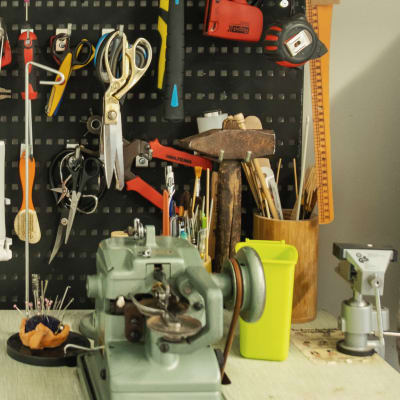 Työtaso, jolla on erilaisia askarteluvälineitä ja työkaluja. Seinällä roikkuu saksia, pihtejä, vasaroita ja vatupassi.