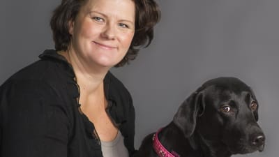 Veterinär Lotta Axelson som svarar på lyssnarnas frågor i Experttimmen, tillsammans med en svart labrador
