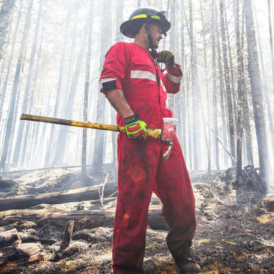 En brandman står i en skog. Han är fotograferad från sidan.