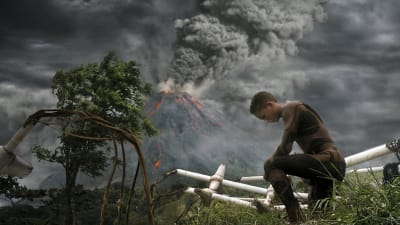 Barn som står på knä, vulkan i bakgrunden. Pressbild