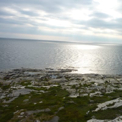 Kylmäpihlajan kallioista rantaviivaa, aurinko paistaa pilvien välistä.