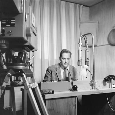 Toimittaja Paavo Noponen studiossa. Radion mikrofonit, mutta televisiokamera kuvaa.  (1959)
