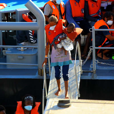 Siirtolainen ja hänen lapsensa rantautuu Maltalaisen laivan kannelta. 