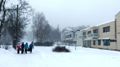 Barn går på en snöig gångled, kontors- och affärshus till höger, en stenkyrka skymtar i bakgrunden.