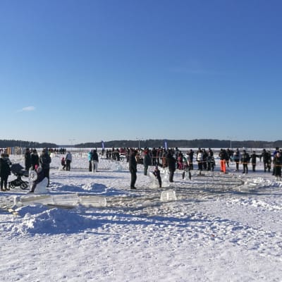 Många människor står på isen. Några barn sitter på isstatyer som åker runt på en iskarusell.