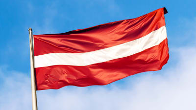 Lettlands flagga framför blå himmel.