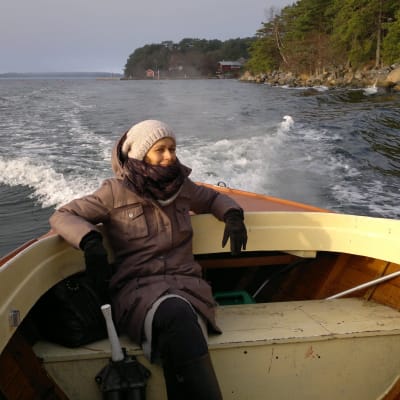 En flicka med kappa, mössa och vantar sitter längst bak på en gammal fiskebåt på väg ut i skärgården i november.