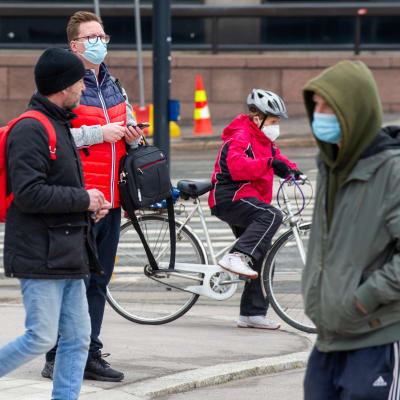 Fotgängare och en cyklist med masker ute i stadstrafiken.