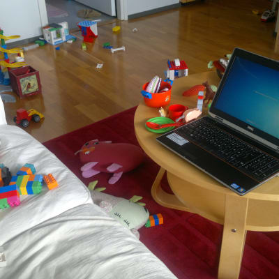 Laptop i vardagsrum fyllt av leksaker.