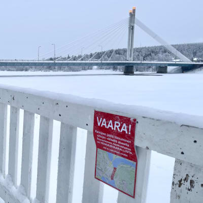 Etualalla puista aitaa, ja heikoista jäistä varottava kyltti. Taustalla Jätkänkynttilä-silta.