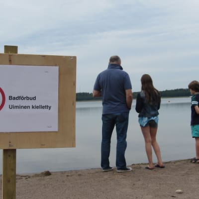 familj på strand invid skylt med badförbud