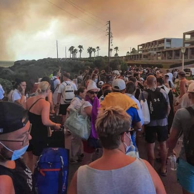 Turister evakueras på Rhodos, himlen är rödgrå av lågor och rök. 