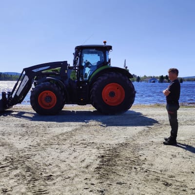 Mies seisoo traktorin vieressä. Taustalla näkyy veden valtaama pelto.
