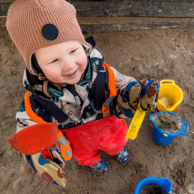 Poika esittelee lapioitaan hiekkalaatikolla.
