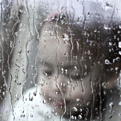 ett litet barn bakom ett fönster i regn