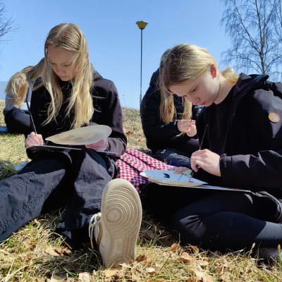 Nuoret istuvat ruohikolla ja piirtävät puistossa.