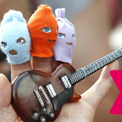 Hand med små ansiktsmasker på tre av fingrarna samt en liten leksakselgitarr i handflatan.