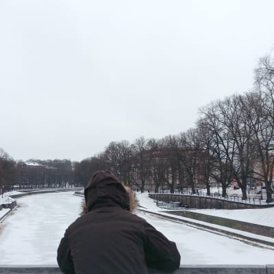 En person i vinterrock står vid Domkyrkobron och tittar ner i Aura å.