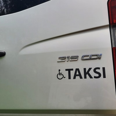 Rullstolssymbol och ordet Taksi i bakändan på en stor taxibil.
