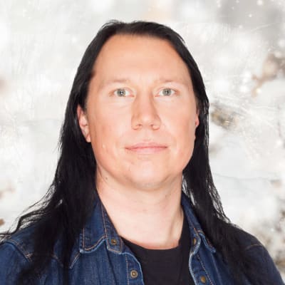 En långhårig man med svart hår ser rakt in i kameran. Bakgrunden är ett vitt vinterlandskap.