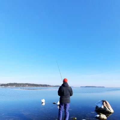 En fiskare står på en sten och fiskar.