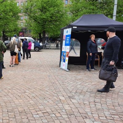 Ett tiotal personer syns köa till en polisbil på Helsingfors järnvägstorg.