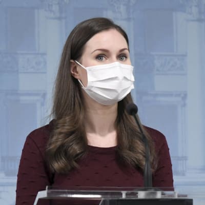 Statsminister Sanna Marin talar vid ett talarpodium. Hon har munskydd på sig.